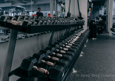 A row of dumbbells in a gym with people working out.